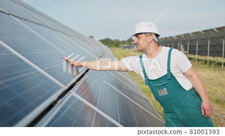 Portrait of proud worker industrial engineer in uniform standing on field with large solar batteries. Ecological farm. Solar power station. People. Sustainable energy. Solar power field. Ecology. Portrait of proud worker industrial engineer in uniform standing on field with large solar batteries. Ecological farm. Solar power station. People. Sustainable energy. Solar power field. Ecology. 81001393