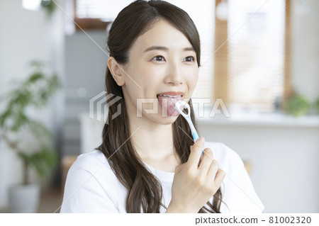 A young woman brushing her tongue in her living room 81002320