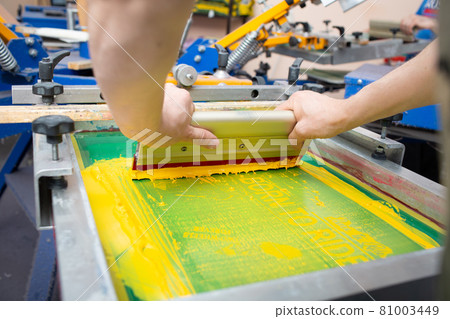 Serigraphy silk screen print process at clothes factory. Frame, squeegee and plastisol color paints Serigraphy silk screen print process at clothes factory. Frame, squeegee and plastisol color paints 81003449