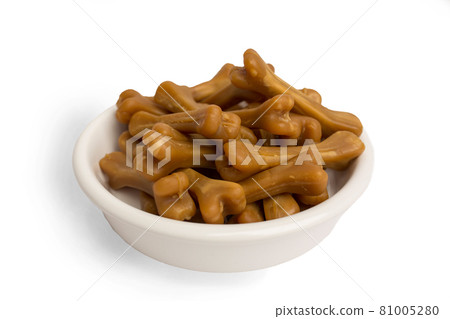 Close-up of brown bones of dog food, in a white food bowl, on a white studio background. 81005280