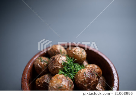 close up of roasted potatoes with herbs in clay bowl on black background 81008996