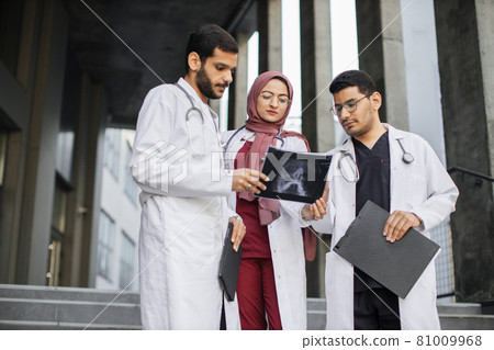 three multi-ethnic doctors and nurse, discussing diagnosis and looking at patient's x-ray scan three multi-ethnic doctors and nurse, discussing diagnosis and looking at patient's x-ray scan 81009968