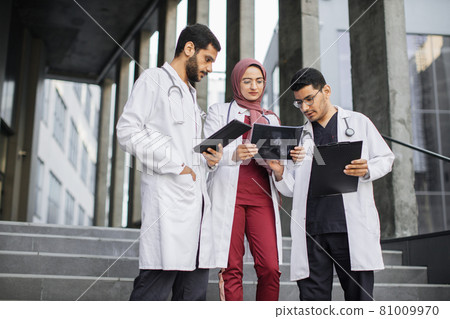 Outdoor shot of team of skilled confident three Asian Indian doctors, looking at patient's xray Outdoor shot of team of skilled confident three Asian Indian doctors, looking at patient's xray 81009970