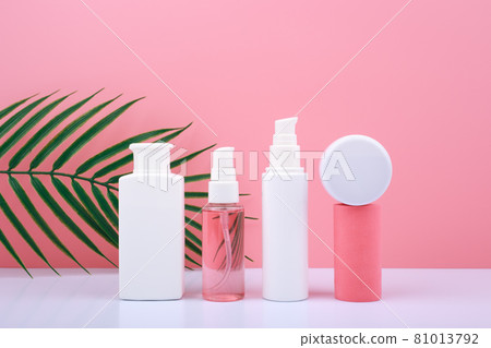 Set of cosmetic bottles with beauty products against pink background with palm leaf 81013792