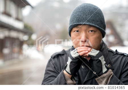 The Asian guy with snow hat stare into the camera and thinking something, Shirakawako valley in the snow season background. 81014365