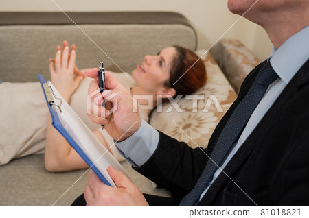 Caucasian woman lies on a couch at a reception with a psychotherapist. An elderly man works as a psychiatrist 81018821