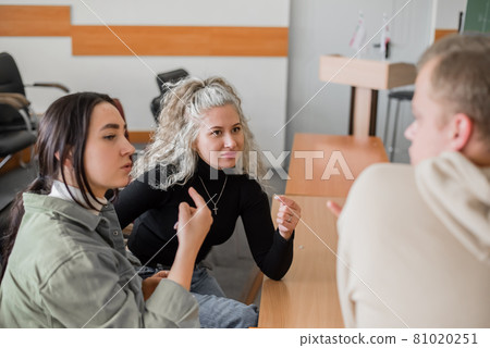 Two girls and a guy are talking in sign language. Three deaf students chatting in a university classroom. Two girls and a guy are talking in sign language. Three deaf students chatting in a university classroom. 81020251
