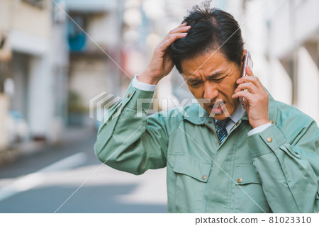 A man in work clothes and a tie gets angry on the phone 81023310