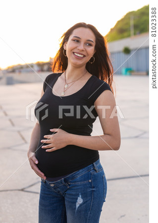 Portrait of hispanic pregnant woman walking on embankment at sunset. Pregnancy and motherhood concept. Portrait of hispanic pregnant woman walking on embankment at sunset. Pregnancy and motherhood concept. 81023388