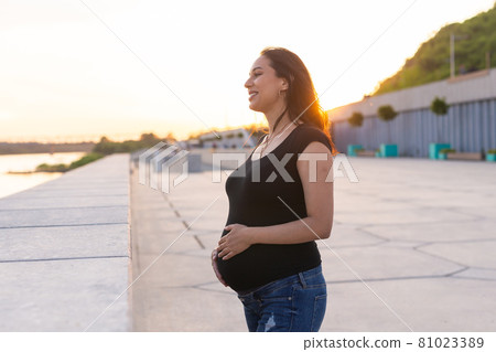 Portrait of hispanic pregnant woman walking on embankment at sunset, copy space. Pregnancy and motherhood concept. Portrait of hispanic pregnant woman walking on embankment at sunset, copy space. Pregnancy and motherhood concept. 81023389