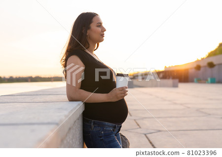 Hispanic pregnant woman drinking take away coffee outdoors. Copyspace. Hispanic pregnant woman drinking take away coffee outdoors. Copyspace. 81023396