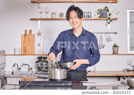 Image of a young man cooking in an apron cooking in the kitchen 81024231
