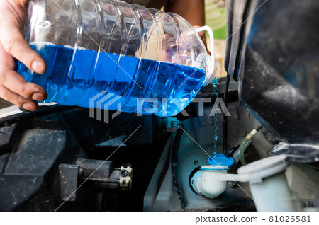Auto mechanic pours windshield washer fluid into the car. 81026581