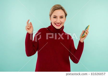 A young cheerful woman in a red sweater with a smartphone on a blue background 81026857