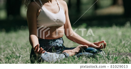 young woman in the lotus position, sitting on the grass . 81029013