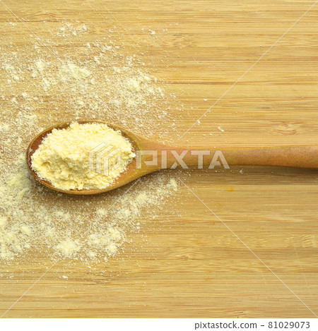 Uncooked corn flour in wooden spoon on bamboo cutting board 81029073