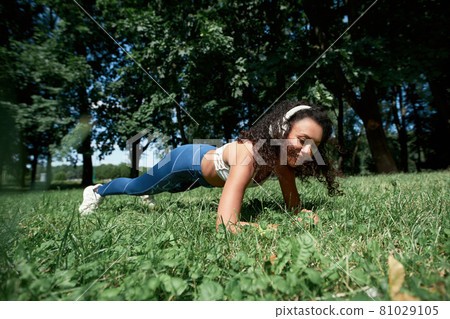 young woman performing a plank exercise in the park. 81029105
