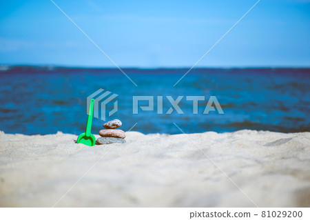 Pretty beach sand toys on dune with gentle waves with sailboat in distance under blue sky Pretty beach sand toys on dune with gentle waves with sailboat in distance under blue sky 81029200