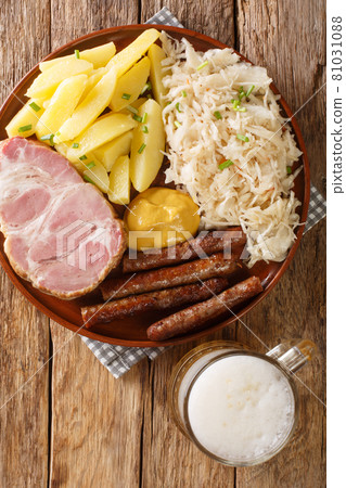 Kassler and sausages served with sauerkraut, boiled potatoes and light beer close-up on wooden background. Vertical top view Kassler and sausages served with sauerkraut, boiled potatoes and light beer close-up on wooden background. Vertical top view 81031088