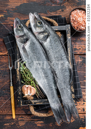 Seabass or sea bass raw fish in a wooden tray with herbs. Dark wooden background. Top view Seabass or sea bass raw fish in a wooden tray with herbs. Dark wooden background. Top view 81032284