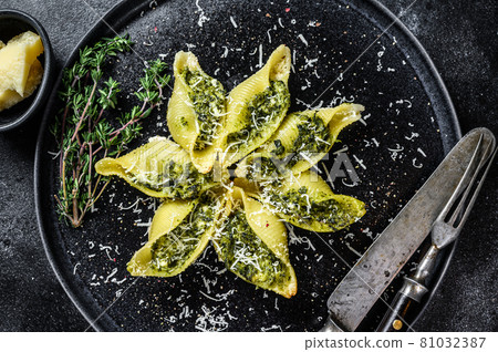 Italian Jumbo shells pasta Conchiglioni stuffed with beef meat and spinach on a plate. Black background. Top view 81032387