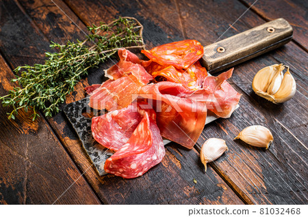 Spanish cured meat salami, jamon, choriso cured sausages on a meat cleaver. Dark wooden background. Top view 81032468