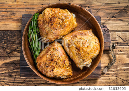 Roasted chicken thighs in a wooden plate with rosemary and herbs. wooden background. Top View 81032603