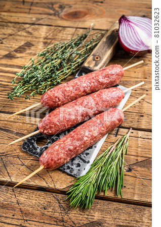 Fresh Raw kofta or lula kebabs skewers on a butcher cleaver with herbs. wooden background. Top view 81032623