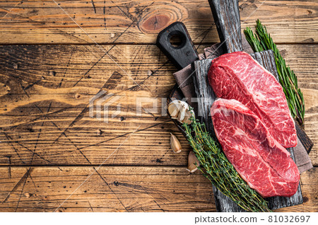 Raw Shoulder Top Blade beef meat steaks on a wooden butcher board with herbs. wooden background. Top View. Copy space 81032697