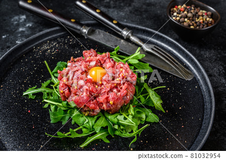 Beef tartare with arugula and quail egg. Black background. Top view 81032954