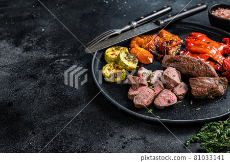 Roasted lamb or goat tenderloin Meat steak in plate with grilled vegetables. Black wooden background. Top view. Copy space 81033141