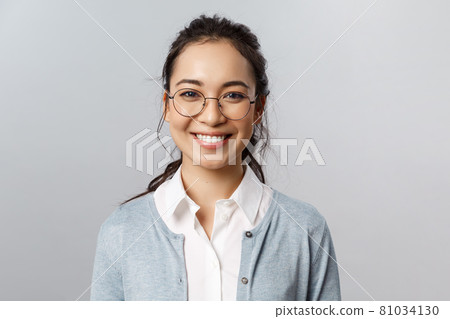 Close-up portrait of attractive, friendly-looking asian female office worker, employee or teacher in glasses, smiling broadly camera with enthusiastic attitude, stand grey background Close-up portrait of attractive, friendly-looking asian female office worker, employee or teacher in glasses, smiling broadly camera with enthusiastic attitude, stand grey background 81034130