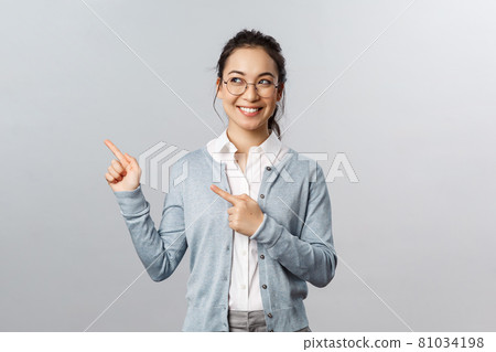 Education, studying and online classes concept. Intrigued, excited happy asian woman in glasses peeking left, smiling and pointing upper corner at advertisement or chart, grey background Education, studying and online classes concept. Intrigued, excited happy asian woman in glasses peeking left, smiling and pointing upper corner at advertisement or chart, grey background 81034198