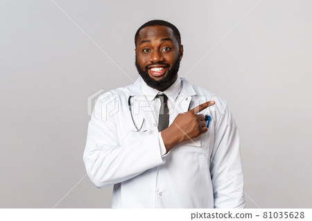 Healthcare, medicine and epidemic concept. Cheerful, friendly-looking african-american male physician explain patients prevention of getting covid19 symptoms, poiting finger right, recommend product 81035628