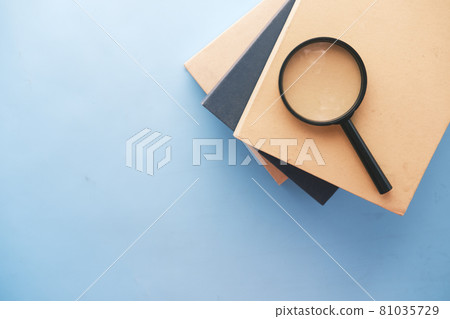 stack of book and magnifying glass on blue background . stack of book and magnifying glass on blue background . 81035729
