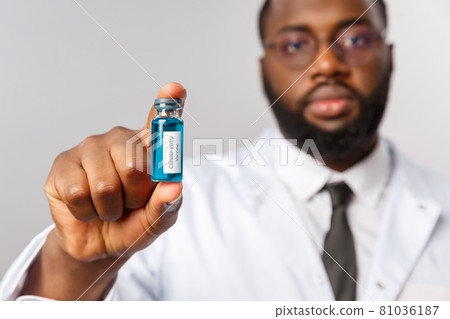 Healthcare, medicine and hospital treatment concept. Serious-looking african-american doctor showing ampule with covid19 vaccine, asking people get vaccinate in clinic, grey background Healthcare, medicine and hospital treatment concept. Serious-looking african-american doctor showing ampule with covid19 vaccine, asking people get vaccinate in clinic, grey background 81036187