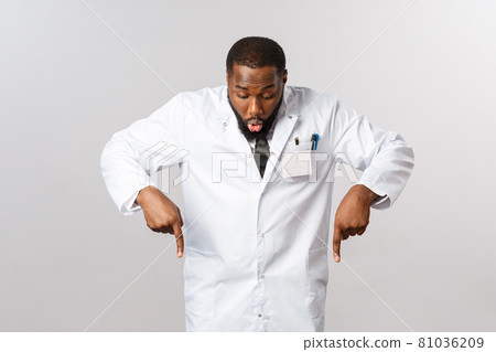 Healthcare, insurance and clinic concept. Amazed and excited african-american doctor in white coat, gasping amused, looking and pointing fingers down at awesome product, great quality, recommend Healthcare, insurance and clinic concept. Amazed and excited african-american doctor in white coat, gasping amused, looking and pointing fingers down at awesome product, great quality, recommend 81036209