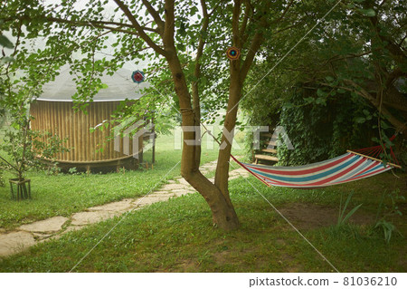 Wooden round summer house among green trees in the morning fog. Wooden round summer house among green trees in the morning fog. 81036210