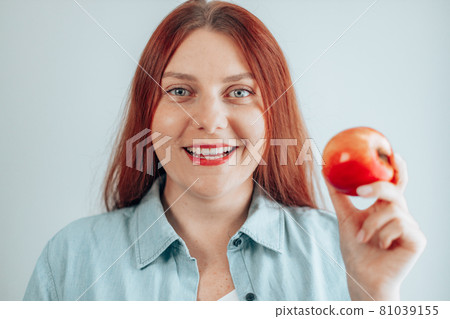 Portrait of a beautiful young woman eating red apple on gray wall background. Healthy nutrition diet. Apple vitamin snack. 81039155