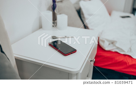 Black smartphone in a red case on the bedside table. Technology and people concept Black smartphone in a red case on the bedside table. Technology and people concept 81039471