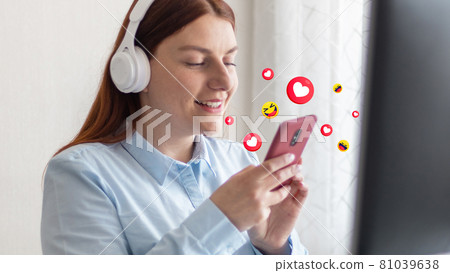 Young beautiful girl listening to music in wireless headphones. Business woman use smartphone for online shopping and typing on keyboard at home office Young beautiful girl listening to music in wireless headphones. Business woman use smartphone for online shopping and typing on keyboard at home office 81039638