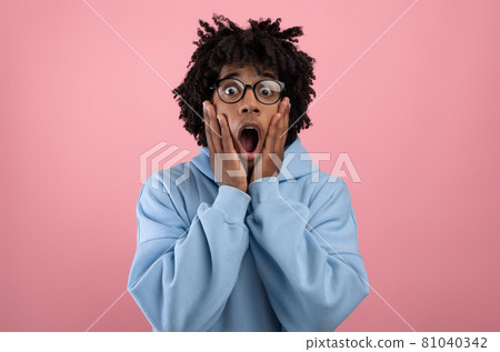 Young black teen guy touching his face, opening his mouth in shock on pink studio background Young black teen guy touching his face, opening his mouth in shock on pink studio background 81040342