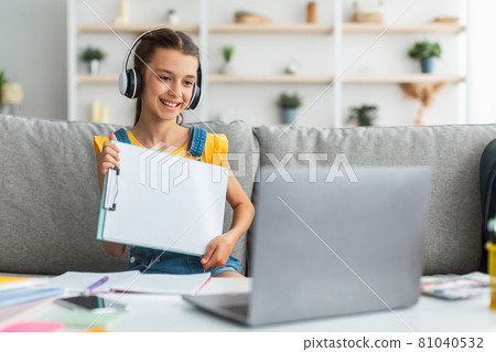 Girl sitting at desk, using pc, showing paper Girl sitting at desk, using pc, showing paper 81040532