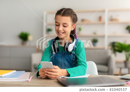 Girl sitting at desk, chatting on cell phone Girl sitting at desk, chatting on cell phone 81040537