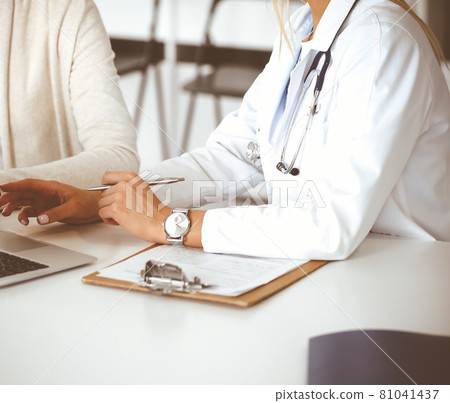 Unknown woman-doctor sitting and communicating with female patient. Physician checks medical history record and exam results, close-up. Healthcare concept Unknown woman-doctor sitting and communicating with female patient. Physician checks medical history record and exam results, close-up. Healthcare concept 81041437