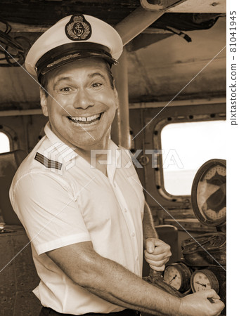 The funny captain standing in the wheelhouse of ship and looking to camera, sepia color. The funny captain standing in the wheelhouse of ship and looking to camera, sepia color. 81041945