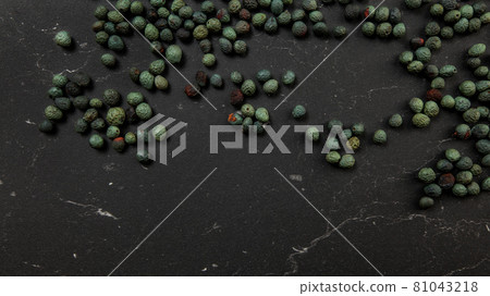 Top down view, Black pepper (Piper nigrum) spice spilled on dark working board. Turkish green / blue peppercorn variant. 81043218