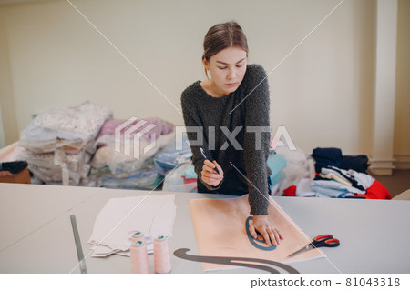Young beautiful seamstress cutter clothing designer with pattern and template in garment factory. 81043318