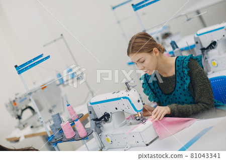 Young beautiful seamstress sews on sewing machine in factory 81043341