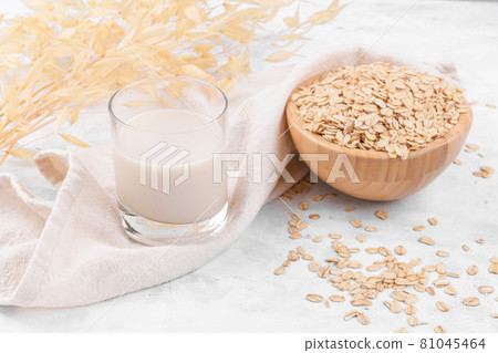 Glass with oat milk and a bowl with oat flake on white stone table Glass with oat milk and a bowl with oat flake on white stone table 81045464